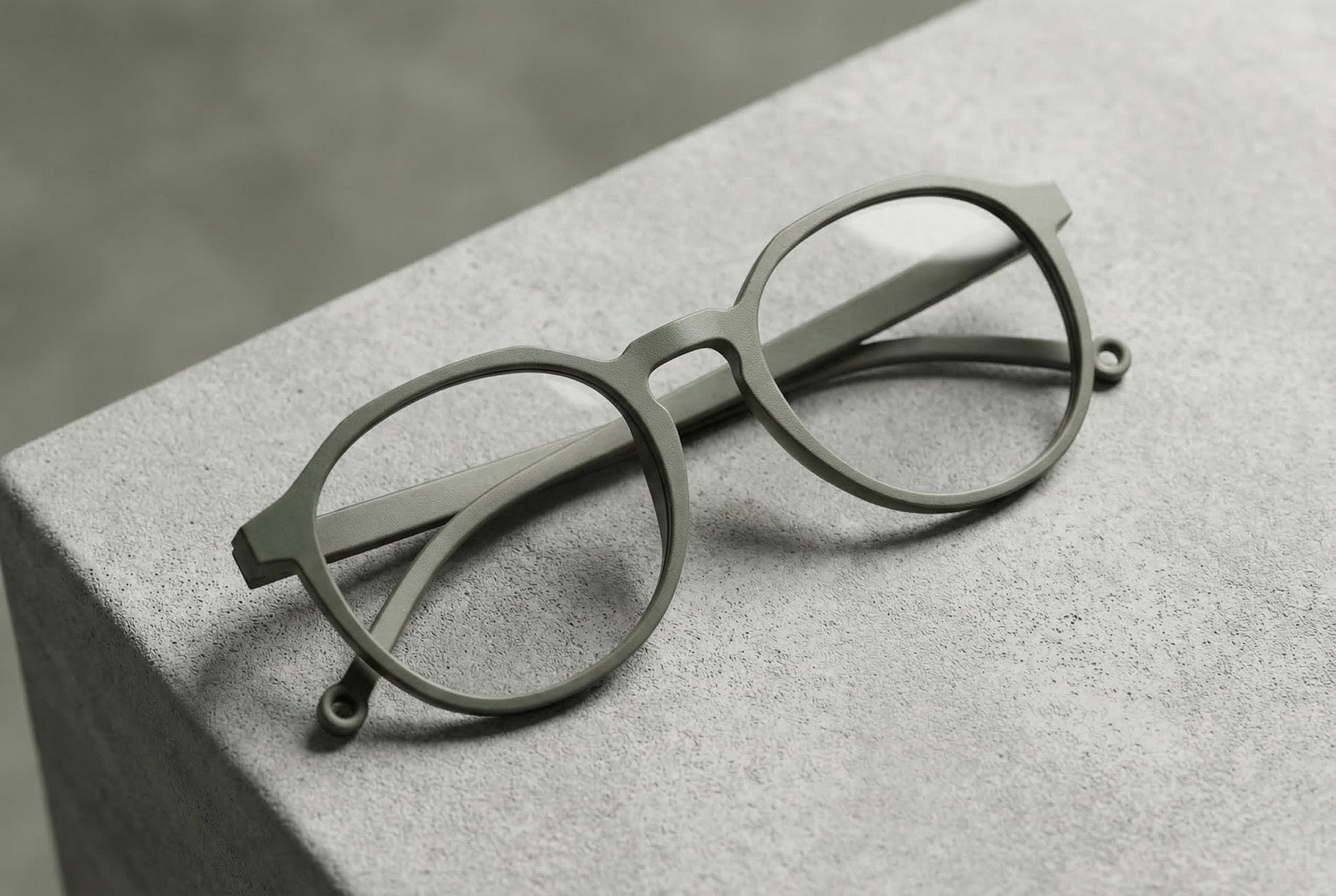 Runde, olivgraue 3D-gedruckte Brille auf strukturierter Oberfläche, reduziert und ruhig inszeniert