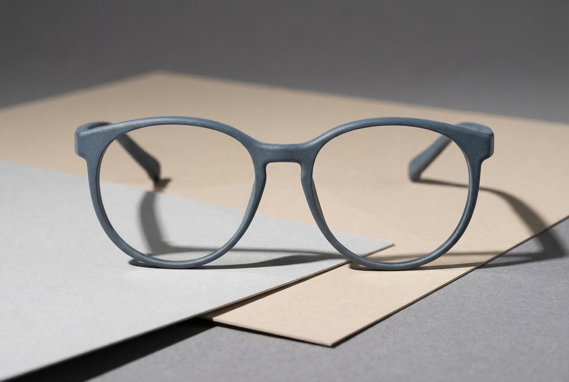 Hellblaue 3D-gedruckte Brille frontal inszeniert auf minimalistischen Papierflächen im Studio